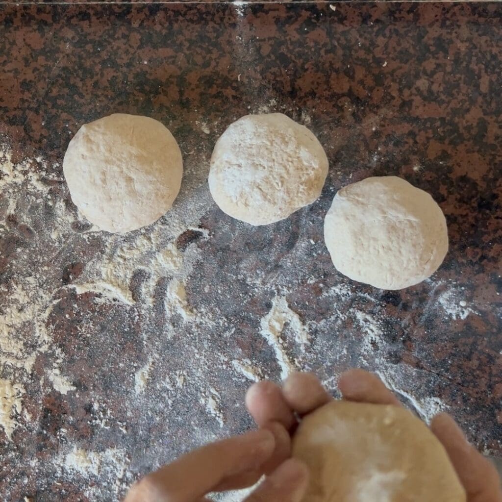 A photo showing 3 readily shaped bread rolls and a hand forming the fourth one.