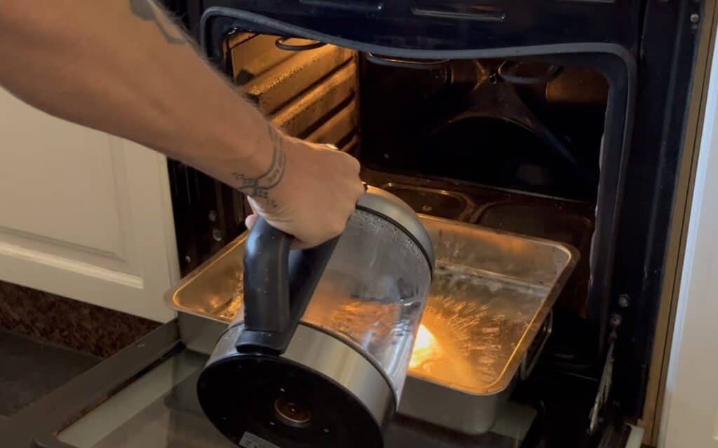 Hot water gets poured into a hot tray in a baking oven to prepare a wet bake 