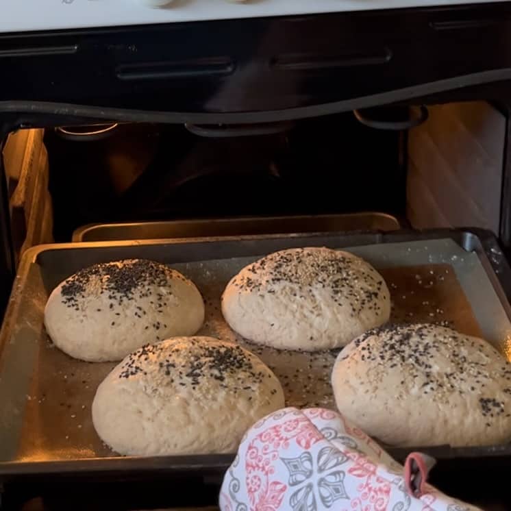 A picture of a baking tray with unbaked breadrolls being put into the hot oven