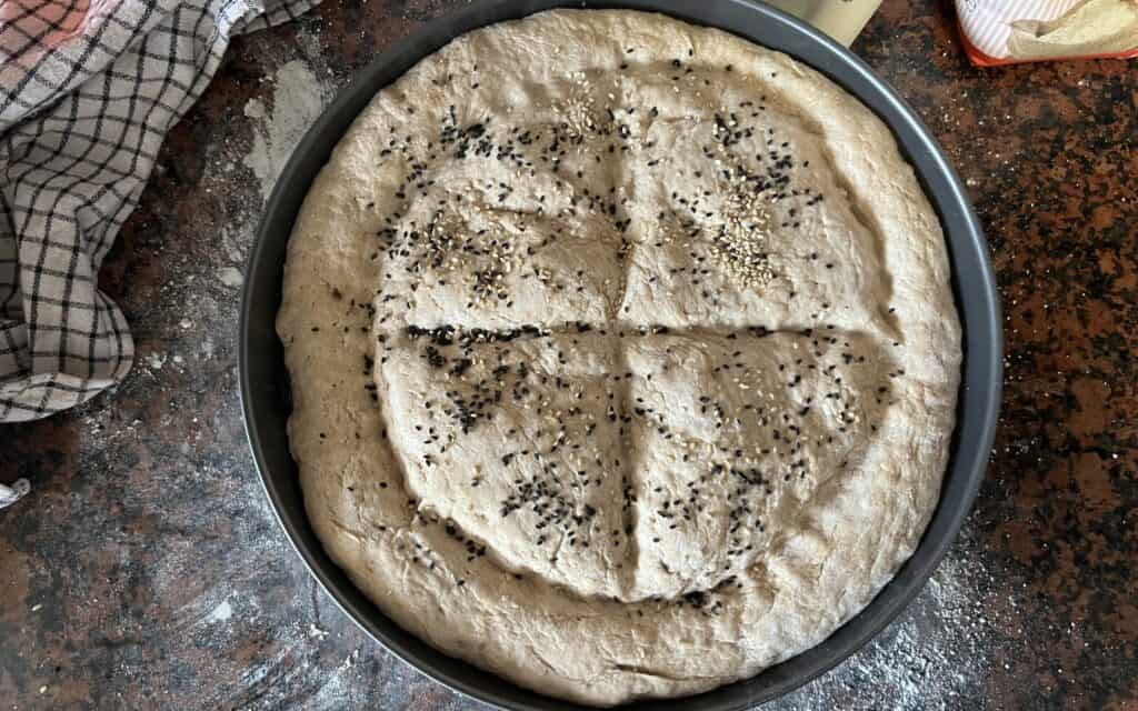 A photo showing a pide dough in a round baking tray, ready to be baked