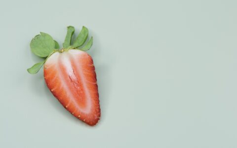 A strawberry cut in half on a mint-colored background.